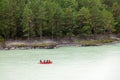 A team of people rafting in orange life jackets on an rubber boat of blue and yellow colors along a mountain river against the