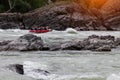 A team of people rafting in orange life jackets on an rubber boat of blue and yellow colors along a mountain river against the