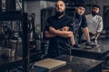 Team of professional bearded cooks dressed in uniforms posing with knives in kitchen.