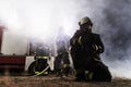 Team of professional firefighters holding water hose in front of a firetruck with smoke in the air. Half silhouette Royalty Free Stock Photo