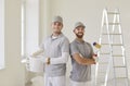 Team of professional painters looking at camera standing in empty room with paint rollers in hands Royalty Free Stock Photo