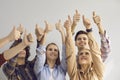 Group of smiling young people raising hands in air and giving thumbs-up all together