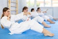 Team of teenage girls in kimono train abdominal muscles and do punches at the same time during karate or judo training