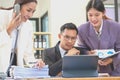 A team of three Asian businessmen is working inside an office where businessmen in black suits are being ordered by their