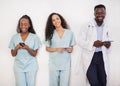 Team of three healthcare professionals lean against wall using digital device