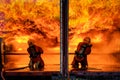 Team of two firefighters wearing full uniform with oxygen tank on back holding pipe spread water and face to wide huge orange hot