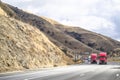 Team of two red big rig semi trucks transporting cargo in dry van semi trailers driving uphill on the mountain highway road in Royalty Free Stock Photo