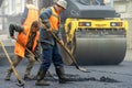 A team of workers with shovels in special yellow clothes is working on the road and laying new asphalt. Repair of asphalt concrete