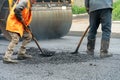 A team of workers with shovels is working on laying new asphalt. Road repairs. Workers with tools next to a roller asphalt stacker Royalty Free Stock Photo