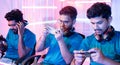 Team of young professional gamers playing live video game on mobile phone by talking on headphones at esports league.