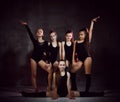 Team of young smiling girls gymnasts in black sport body and uppers posing over grey background