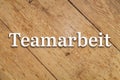 `Teamarbeit` white text on a wooden background. Translation: Team work