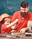 Teamwork and assistance concept. Father, parent with beard teaching little son to use tool screwdriver. Boy, child busy Royalty Free Stock Photo