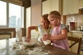 Teamwork. Cute little girl in apron helping her brother while preparing dough for cookies together on the kitchen table Royalty Free Stock Photo