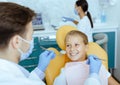 Male doctor in white coat with rubber gloves and protective mask treats teeth of smiling girl in chair