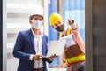 Teamwork foreman man and woman wearing protection face mask and safety helmet using laptop and holding clipboard. Royalty Free Stock Photo