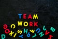 Teamwork training concept. Text teamwork lined with colored letters near toy letters on black background top view space