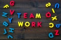 Teamwork training concept. Text teamwork lined with colored letters near toy letters on dark wooden background top view