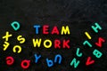 Teamwork training concept. Text teamwork lined with colored letters near toy letters on black background top view space