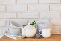 Teapot, cups and other tableware on the wooden table near the brick wall.