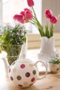 Teapot with dots and vases with beautiful spring flowers on the wooden table. Decoration for home interior.Forget-me-not