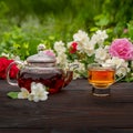 Teapot and an elegant glass cup among flowering rose and jasmine.