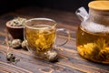 Teapot and glass cup with blooming tea flower inside on a wooden table Royalty Free Stock Photo