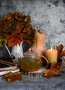Teapot with sea buckthorn tea, bouquet of maple leaves, books, burning candle on the table. Cozy home autumn still life Royalty Free Stock Photo
