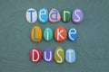 Tears like dust, sad phrase composed with multi colored stone letters over green sand