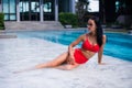 Teasing young smiling woman brunette beauty with red bikini rests laying on wet poolside marble enjoying summer in the Royalty Free Stock Photo