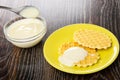 Teaspoon with condensed milk above bowl, cookies with milk in saucer on wooden table Royalty Free Stock Photo