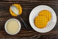 Spoon with condensed milk on cookie, bowl with condensed milk, waffle cookies in saucer on wooden table. Top view Royalty Free Stock Photo