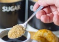 A teaspoon full of demerara sugar,being put into into a small,white cup of hot espresso coffee,in a domestic kitchen,