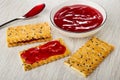 Spoon with jam, bowl with cherry jam, sandwich from crackers with flax seeds, cookie with jam on table