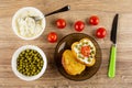 Spoon in jar with soft cheese, tomato, bowl with green peas, sandwich from dairy toasts in saucer, knife on table. Top view Royalty Free Stock Photo