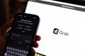 Tech guy trying out Grok in mobile phone with the laptop screen showing Grok logo, an generative, conversational, neural network,