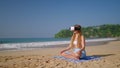 Woman in VR headset meditates on sandy beach, virtual reality transport to exotic locale for mindfulness. Tech offers