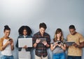 Teched out youth of today. Studio shot of a group of young people using wireless technology against a gray background.