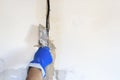 . technical hole in it is an electrical wire. the wall is white. Master with a spatula and mortar covers the cable