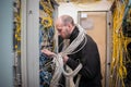 The technician, all wrapped in cables, connects the wires in the rack of the server room. A man works with Internet equipment in a Royalty Free Stock Photo
