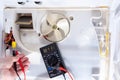 A technician checks an electrician with a digital multimeter in refrigerator fridge. Inside refrigerator repair