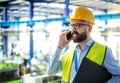 Technician or engineer with hard hat standing in industrial factory, using telephone. Royalty Free Stock Photo