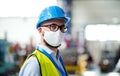 Technician or engineer with protective mask and helmet standing in industrial factory.