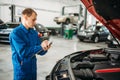 Technician fills check list, car with opened hood Royalty Free Stock Photo
