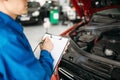 Technician fills check list, car with opened hood Royalty Free Stock Photo