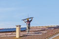 A technician lifts a solar panel over his head as he prepares to mount it on the roof of a red-tiled house Royalty Free Stock Photo