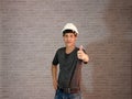 Technician man ware white helmet with dark grey T-shirt and denim jeans standing and left hand thumbs up. Royalty Free Stock Photo