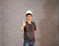 Technician man ware white helmet with dark grey T-shirt and denim jeans standing and right hand thumbs up. Royalty Free Stock Photo