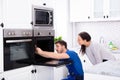 Technician In Overall Fixing Oven In Kitchen