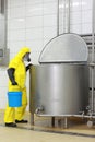 Technician in protective coveralls with blue bucket at opened industrial process tank